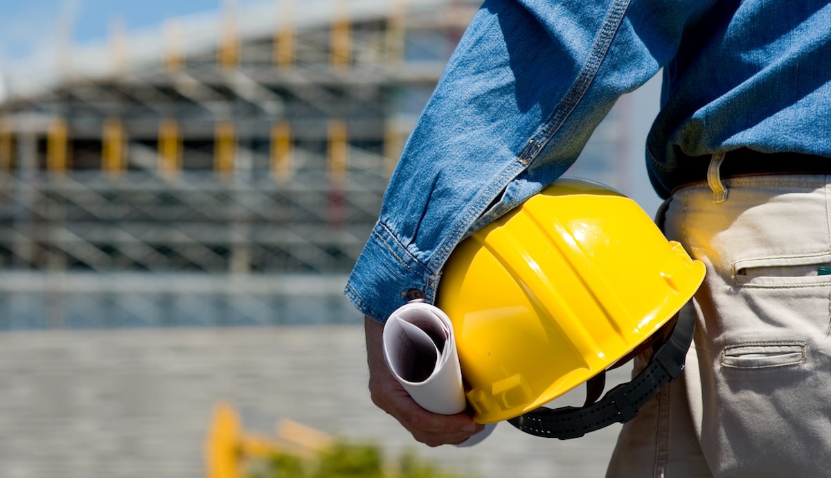 Foreman on construction site holding yellow hard hat with back turned