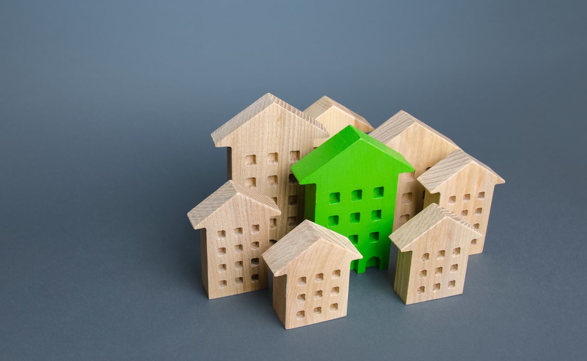 Green model house surrounded by wooden houses with gray background