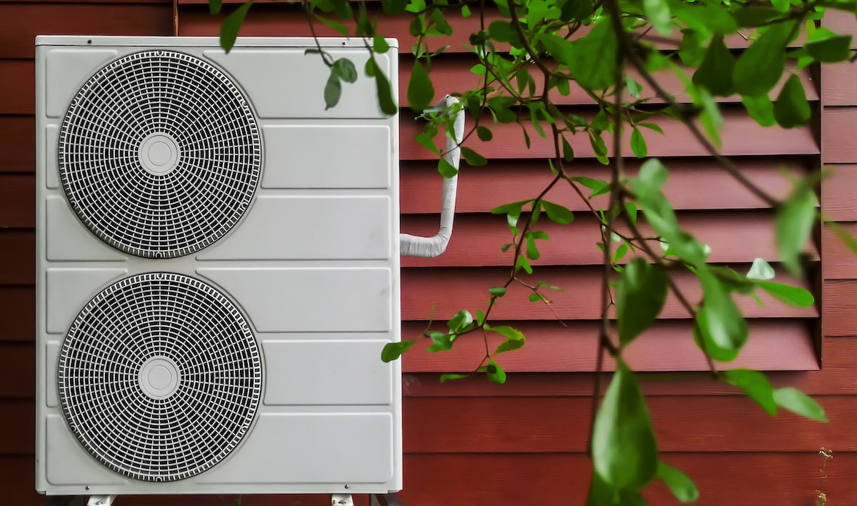 Electric heat pump against exterior wall of red residential home