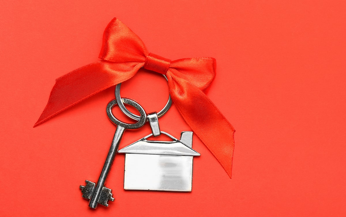 Silver house keys wrapped with red ribbon against red background