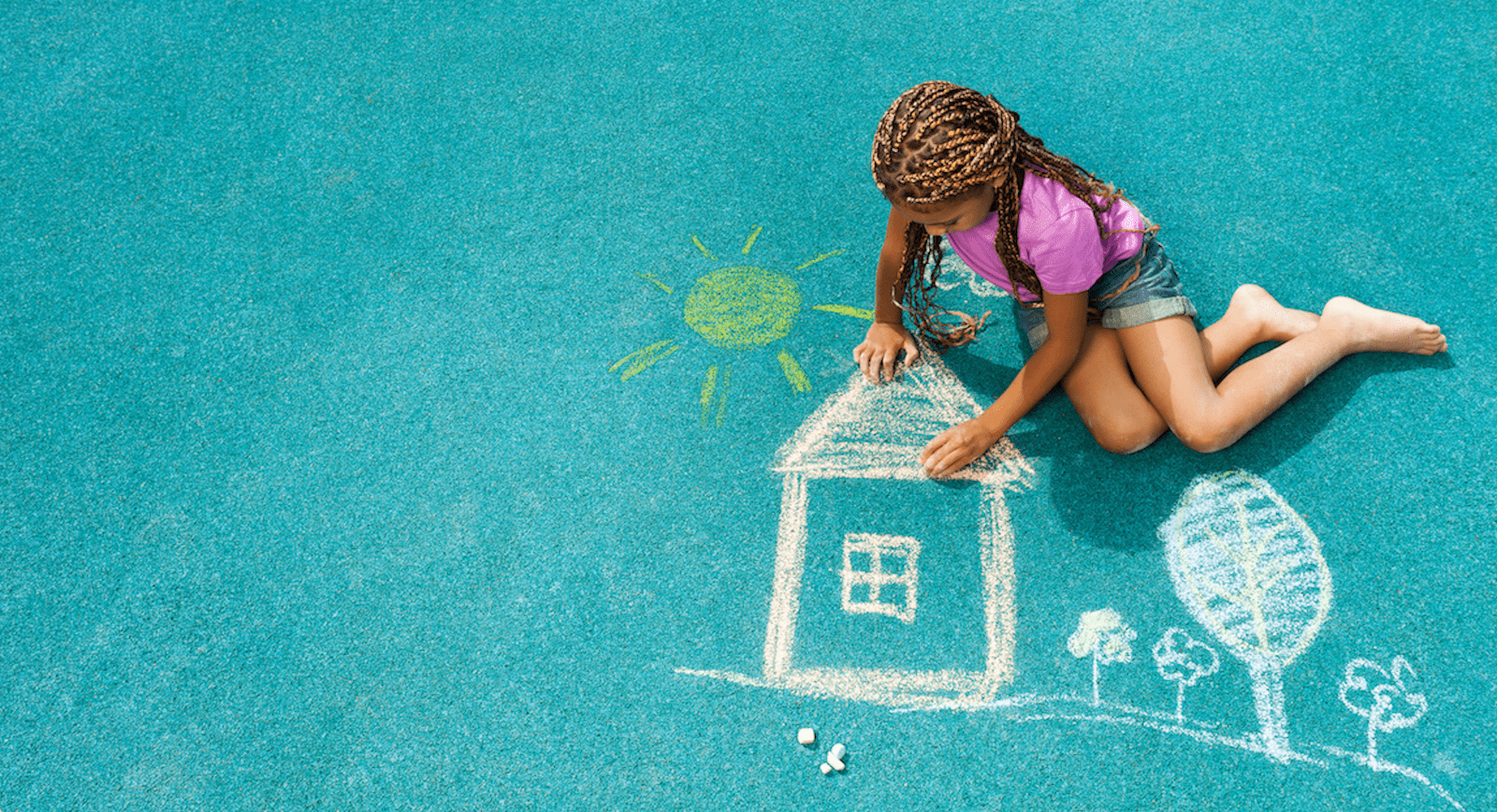 Girl drawing house on pavement with chalk