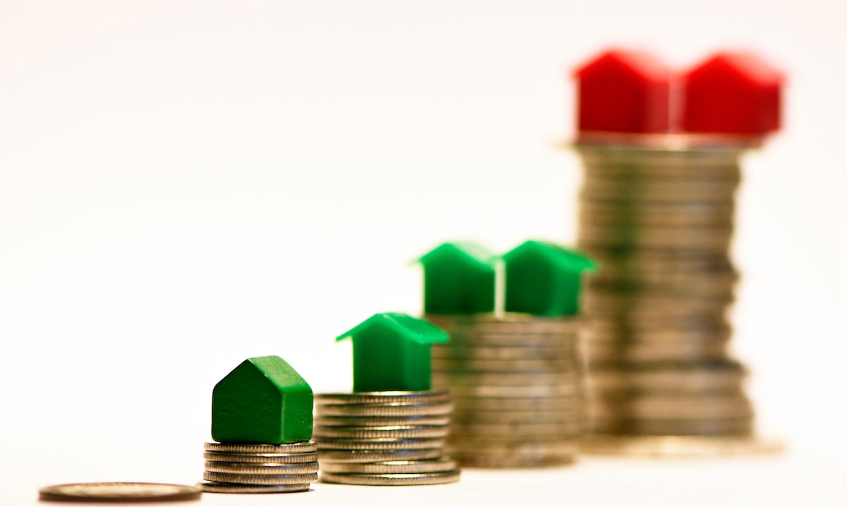 Green and red houses on different sized stacks of coins representing homeownership gap