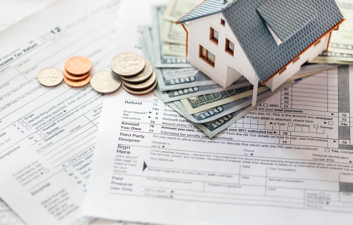 Small house, stack of cash, and coins on top of tax forms