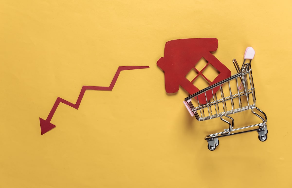 Red house falling out of small shopping cart next to dropping red arrow with yellow background