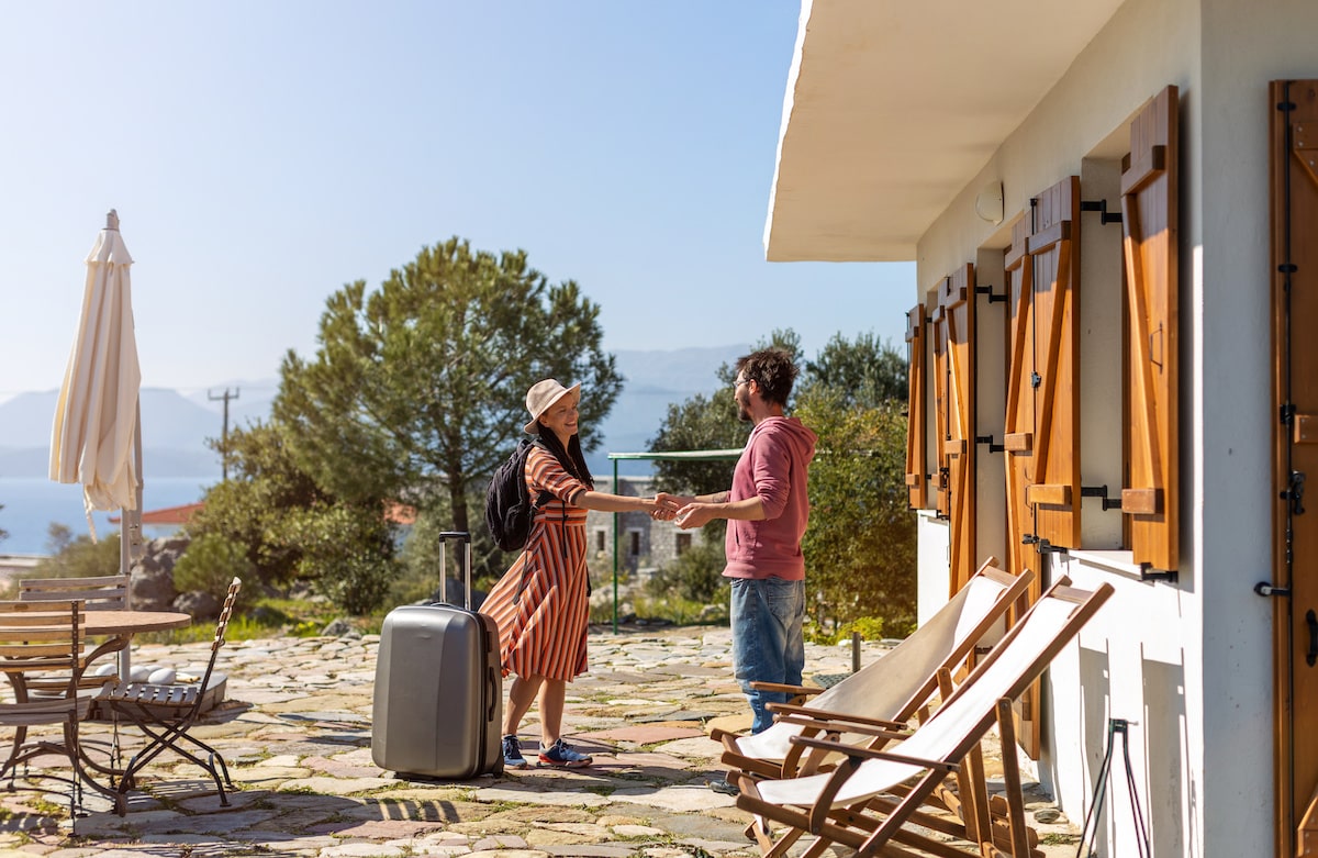 Homeowner greeting guest with suitcase outside of vacation rental 