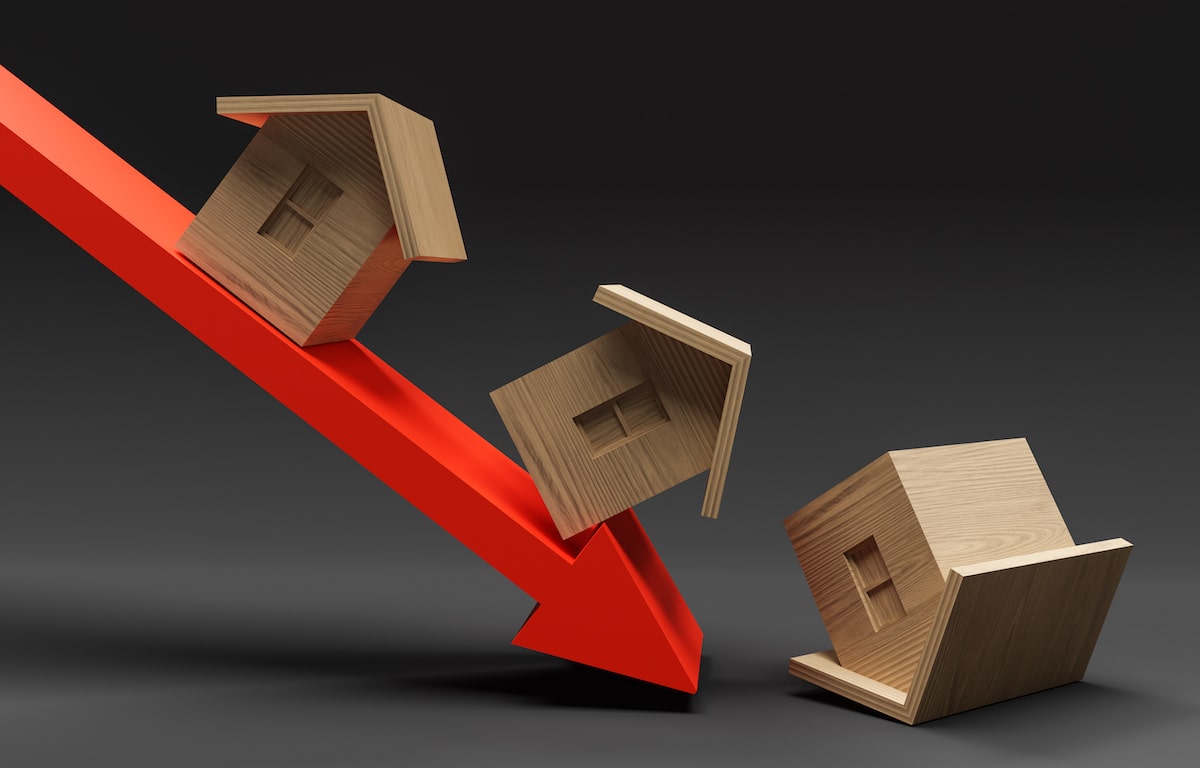 Wooden houses falling against declining red arrow