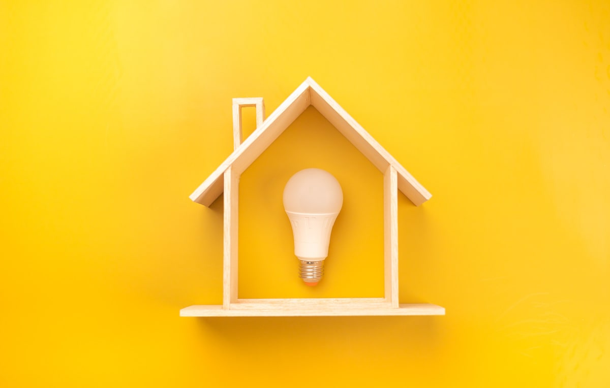Light bulb inside of small wooden house against yellow background