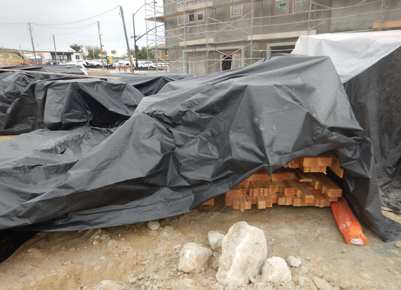 lumber on jobsite covered by plastic tarp for protection from weather