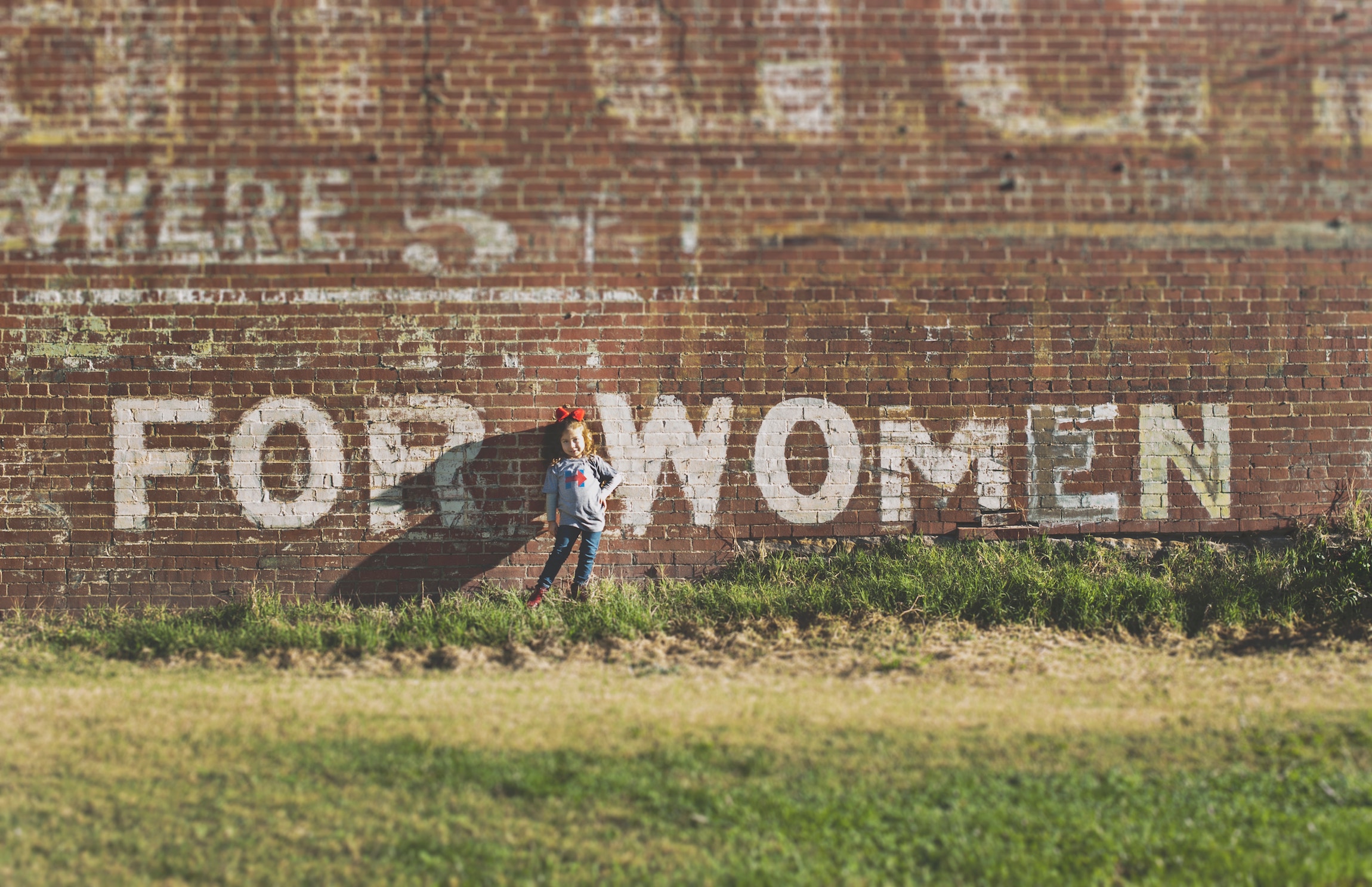 Little girl in front of brick wall that says "for women"