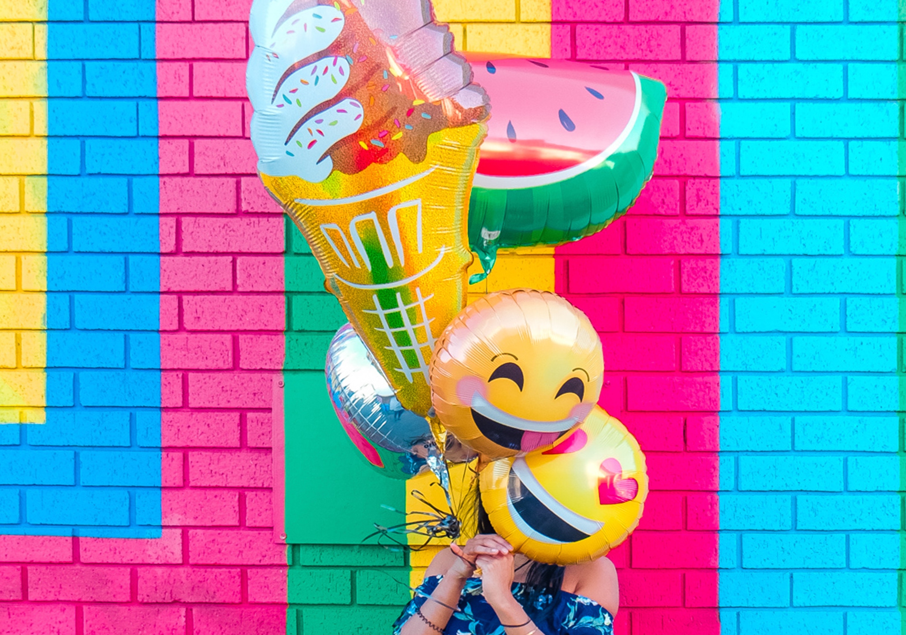 Person holding helium balloons in front of colorful brick wall