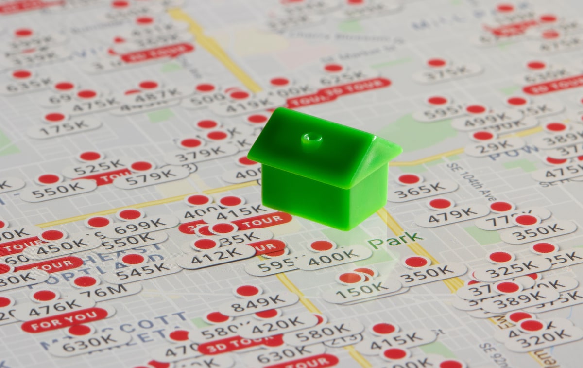 Small green house model on top of map of real estate listings
