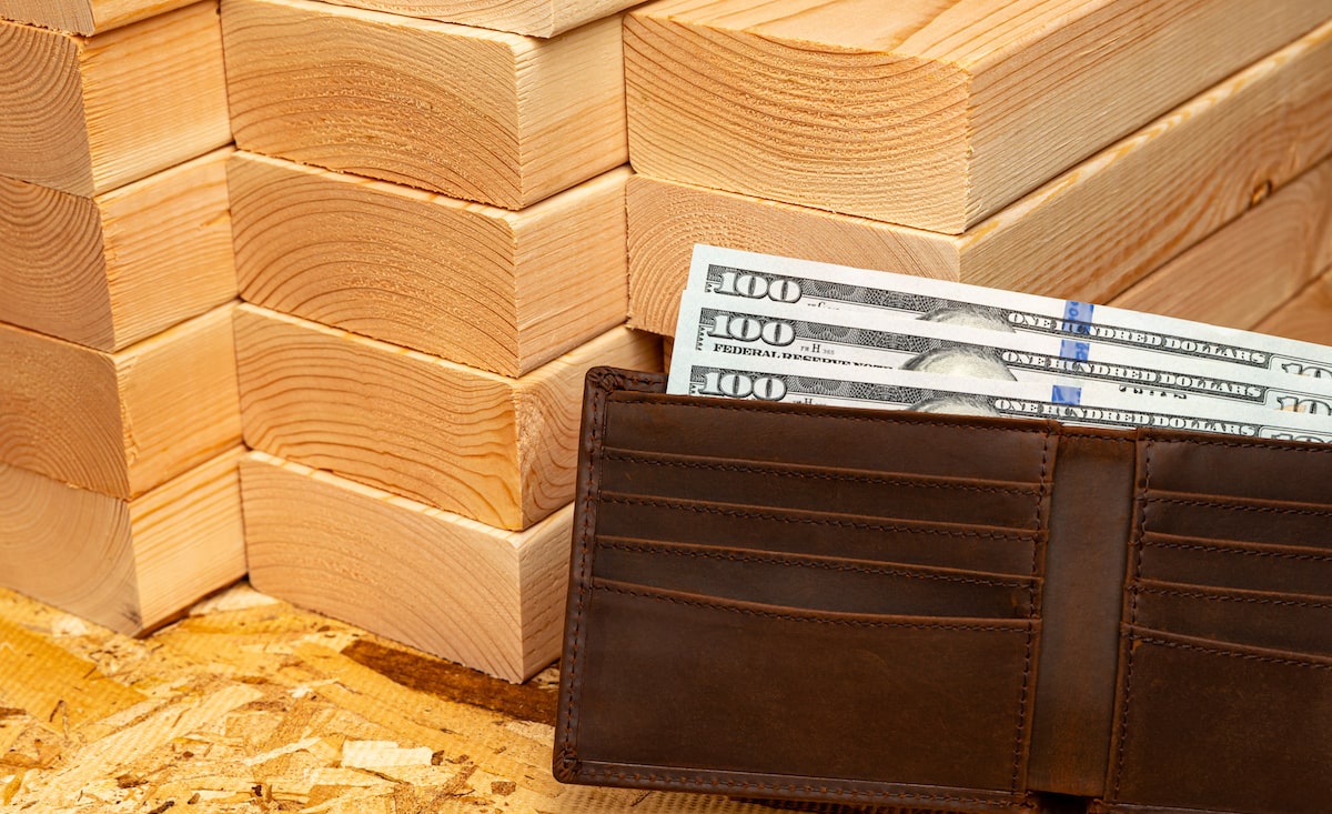 Stack of lumber next to wallet full of hundred dollar bills