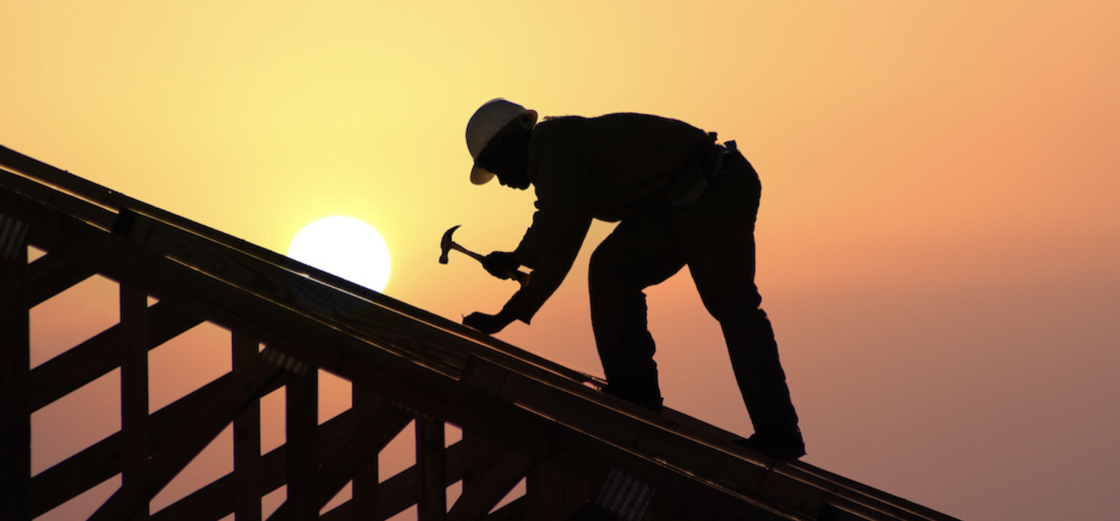 Man using hammer building home roof at dawn