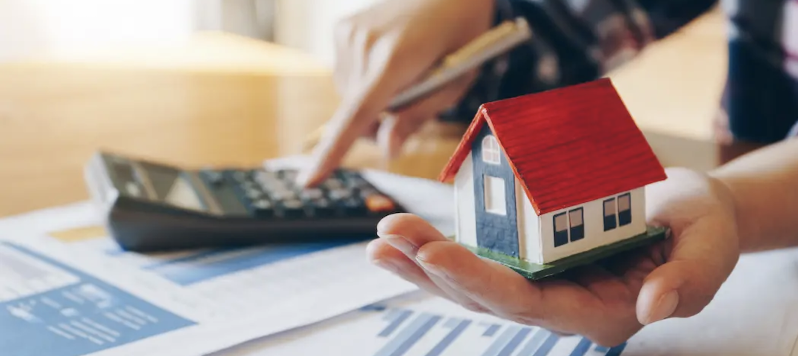 Man holding home figurine in one hand while using calculator to calculate home mortgage with the other hand 