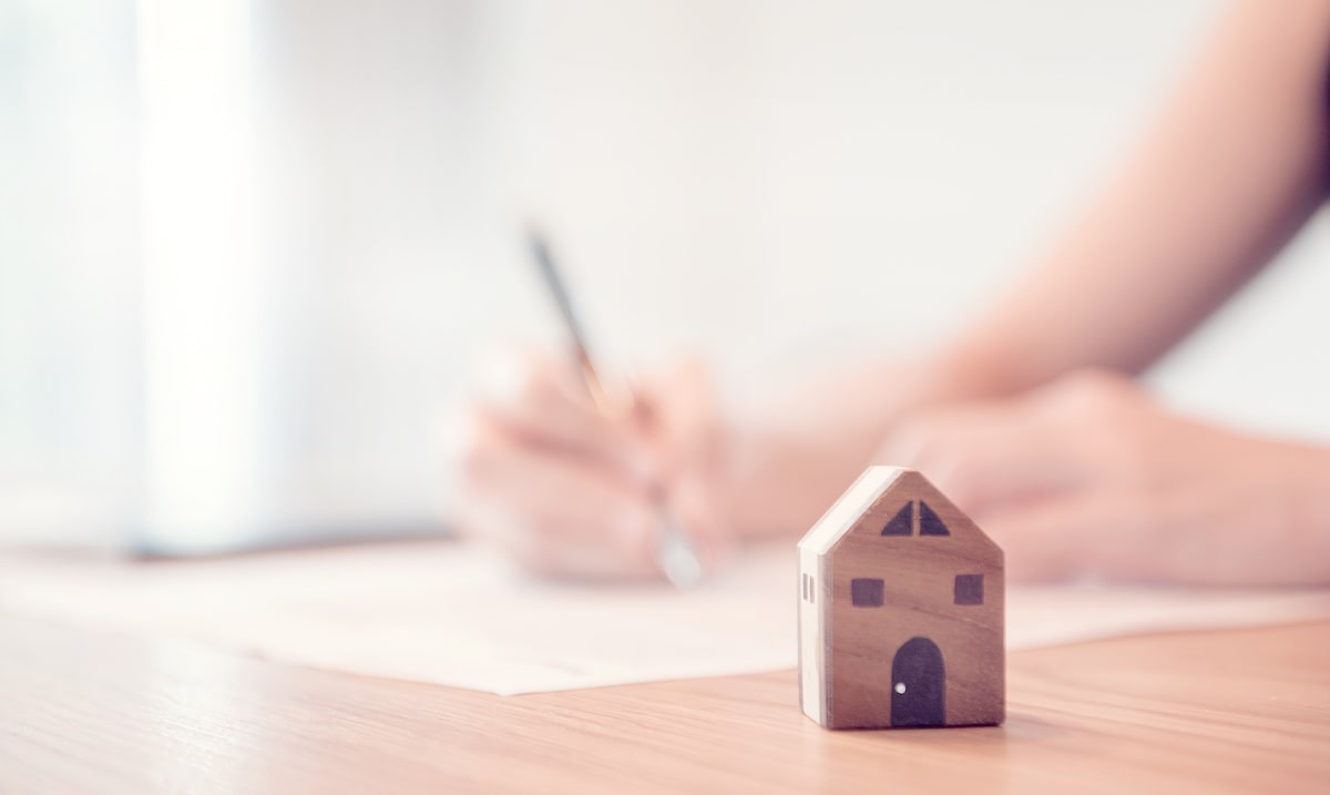 Person signing paper next to small wooden house model