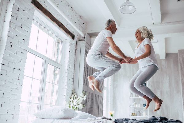 Older couple jumping on bed in apartment