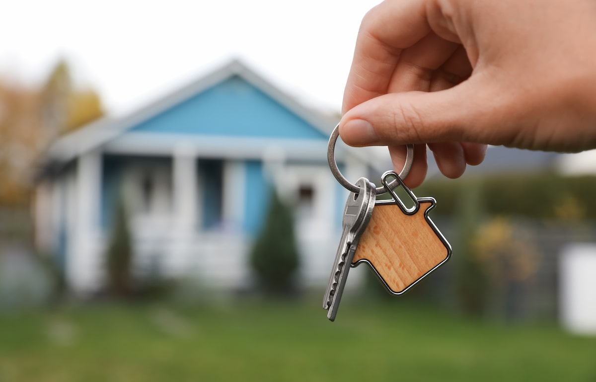 Person holding up house keys with blue house in background