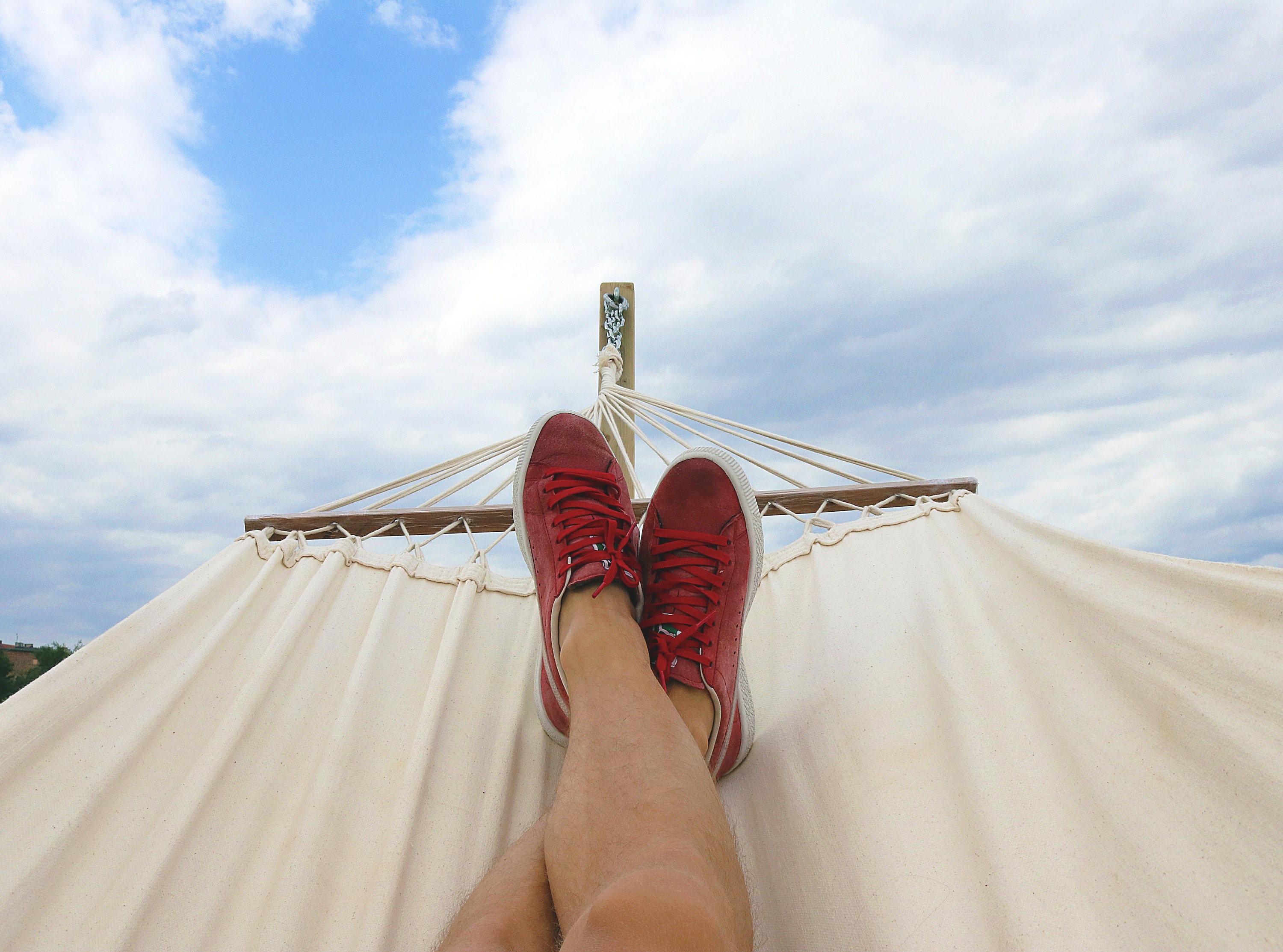 Man in hammock with red shoes looking up at clouds in blue sky