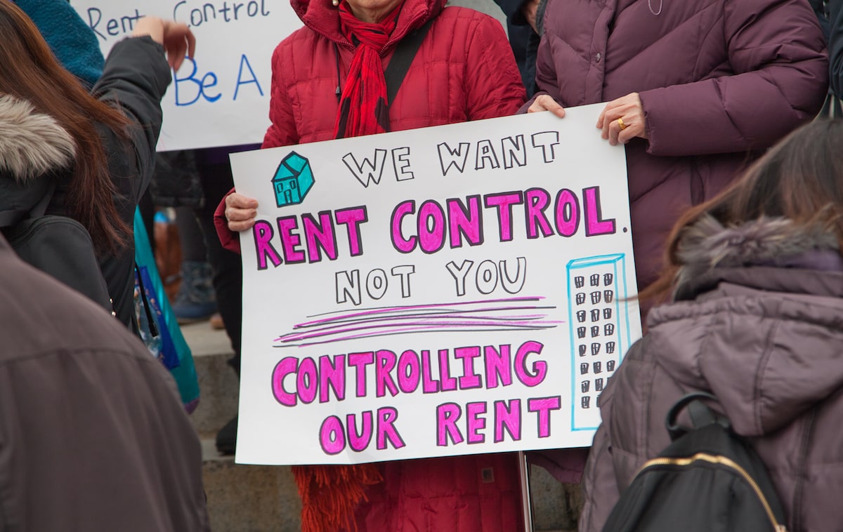 Protestor holding sign that reads "We want rent control, not you controlling our rent." 