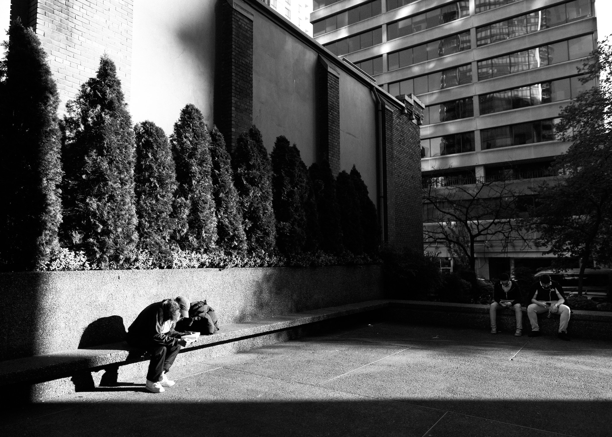 Three people on benches in city in b/w photo