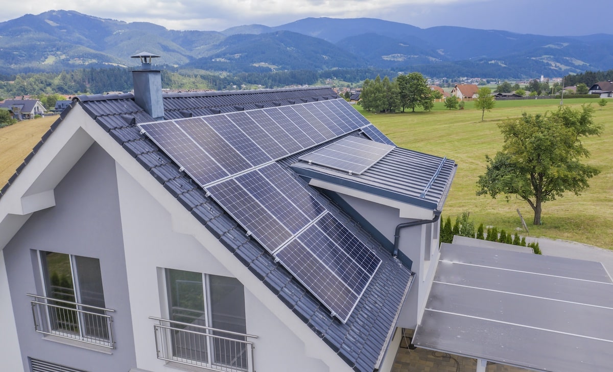 Solar panels on roof of gray house surrounded by fields and mountains