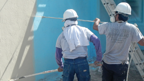 Two construction crew members painting a stucco wall on the jobsite