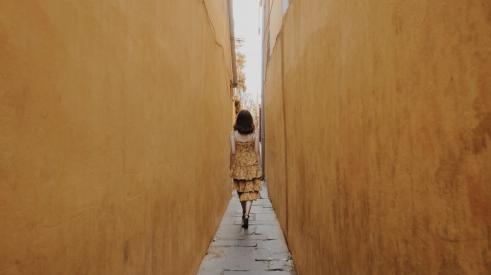 Woman walking in narrow space between two tall walls