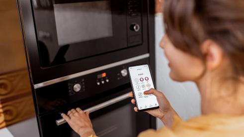 Woman holding smart phone and using smart oven appliance