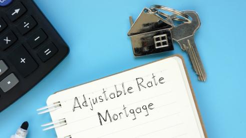 Notepad that says adjustable rate mortgage next to house keys and laptop