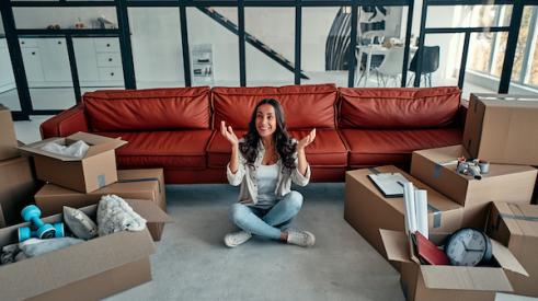 Woman sitting on floor of new house smiling with boxes around 