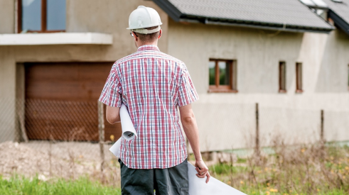 Home builder walking toward house with plans in hand