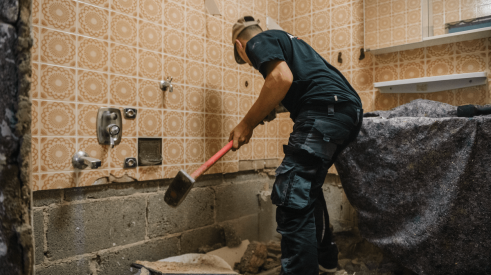 Worker swings sledge hammer to demolish bathroom for home remodel