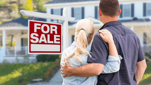 Couple standing together next to for-sale sign looking at home