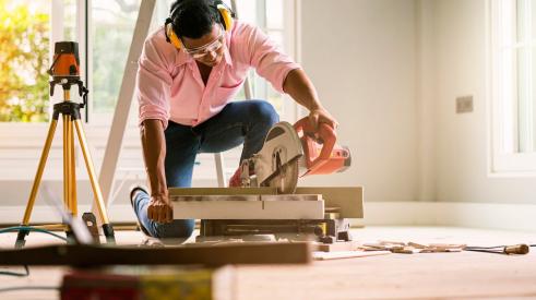 A man is using a circular saw to cut wood for a home building project.