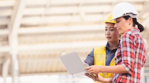 Two women review construction plans on laptop