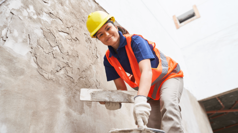 Woman construction worker applying stucco to wall on jobsite