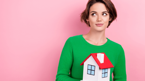 Woman renter holding model house in her hands gives a sidelong glance