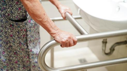 Old woman holding handrail next to bathroom sink
