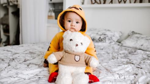 Child seated on bed with teddy bear