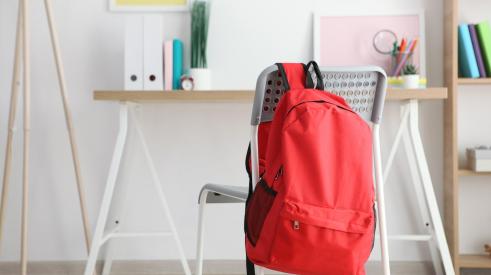 Red backpack hanging on chair in bright home workspace