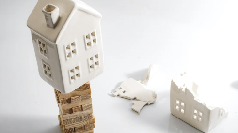 Ceramic model house teetering on Jenga blocks, danger of falling and breaking