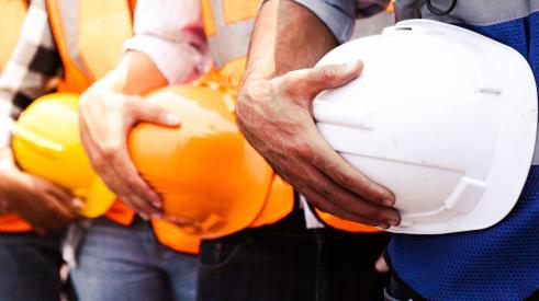 Row of tradespeople holding construction hard hats