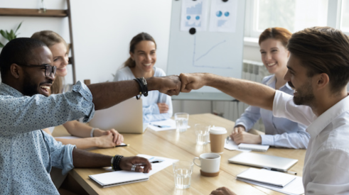 Coworkers fist bumping at a conference table show teamwork and positive company culture