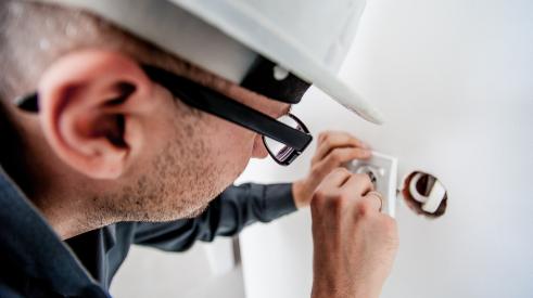 construction worker wearing hard hat installing electrical outlet in wall