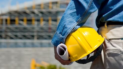 Foreman on construction site holding yellow hard hat with back turned