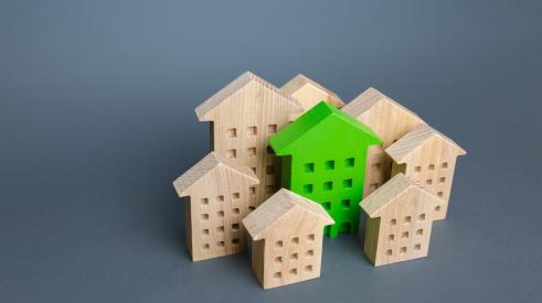 Green model house surrounded by wooden houses with gray background