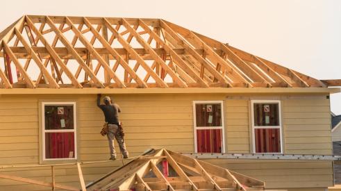 Home builder standing on roof of new house under construction