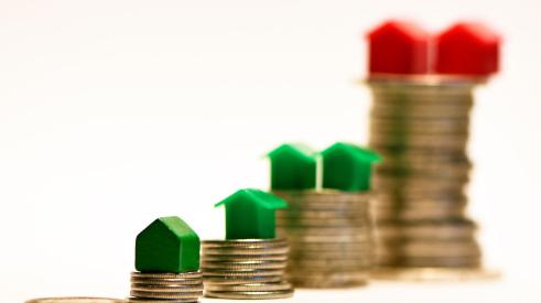 Green and red houses on different sized stacks of coins representing homeownership gap