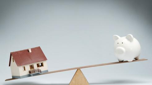 House and piggy bank on uneven balance