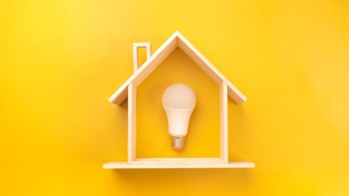 Light bulb inside of small wooden house against yellow background